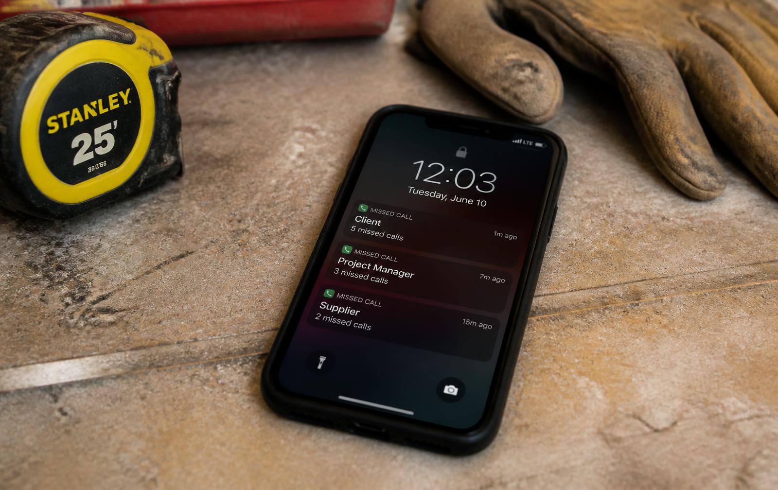 A contractor's phone on a work surface showing missed calls, next to a tape measure and work gloves.